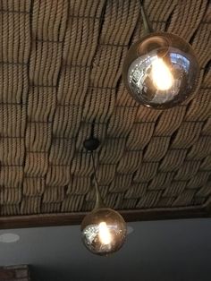 three lights hanging from the ceiling in a room with rafters and woven wallpaper