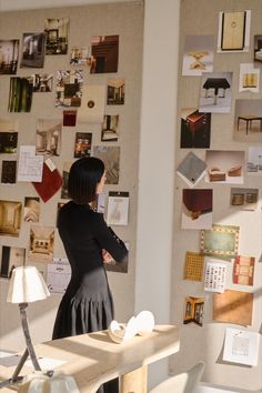 a woman standing in front of a wall covered with pictures and papers on the wall