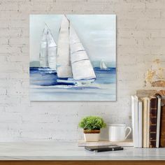 two sailboats in the ocean on a white brick wall above a table with books