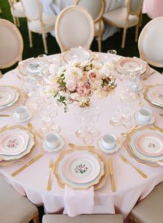 the table is set with pink and white plates, silverware, and flowers in vases