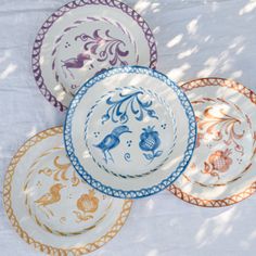 four plates with different designs on them sitting on a white tablecloth under a tree