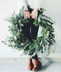 a woman is holding a wreath with greenery on it and her hands are in the center