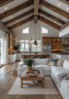 a living room filled with lots of furniture and wooden beams on the ceiling over a kitchen