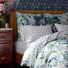 a bed with blue and white sheets, pillows and flowers on the headboard next to a night stand