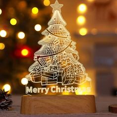 a laser cut christmas tree on a wooden stand next to a pine cone with lights in the background