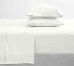 two white pillows on top of a bed with sheets and pillowcases in the background