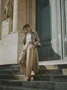 a woman is walking down some steps talking on her cell phone and wearing a trench coat