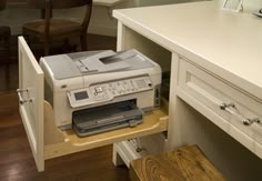 a printer sitting on top of a wooden drawer in a kitchen next to a desk