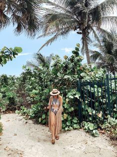 a woman in a bathing suit and hat walking down a path next to palm trees