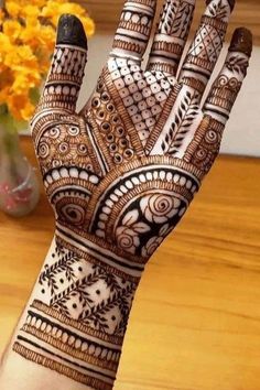 a hand with henna on it sitting next to a vase filled with yellow flowers