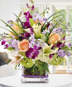 a vase filled with lots of different colored flowers on top of a white table next to a window