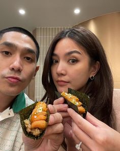 two people holding food in their hands and posing for the camera with one person looking at the camera