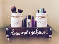 two mason jars with makeup brushes in them are sitting on a shelf that says, kiss and make - up