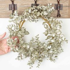 a wreath is hanging on a wall with two hooks and one hand holding it up