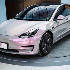 a white tesla electric car parked on top of a circular floor in front of a building