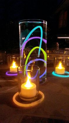 some lit candles sitting in front of a glass vase with neon lights on the outside