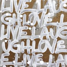 the words live laugh love have written in white spray paint on a brown and tan background