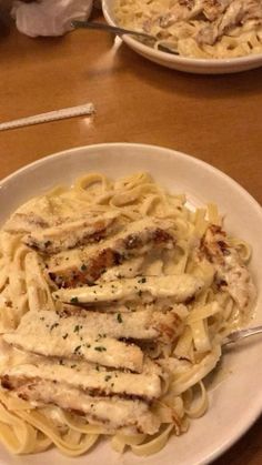 two plates of pasta with chicken and sauce on the table next to silverware in front of them