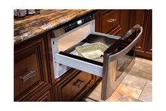 an open dishwasher drawer in a kitchen with marble counter tops and wooden cabinets