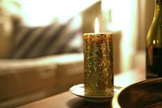 a lit candle sitting on top of a wooden table next to a bottle of wine