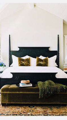 a bedroom with a large bed and lots of pillows on the headboard, along with a bench