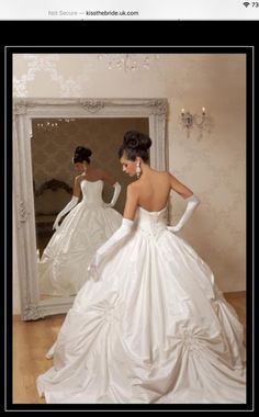 a woman in a white wedding dress looking at herself in the mirror with her hands on her hips