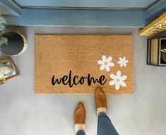 a person standing in front of a welcome mat with daisies on it and the words welcome