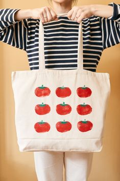 a woman holding a tote bag with tomatoes on it