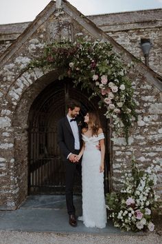 a bride and groom are standing in front of an archway with flowers on the side