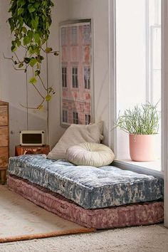 a bed sitting next to a window with a plant on it's headboard