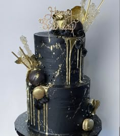 a three tiered black and gold cake with lots of decorations on the top layer