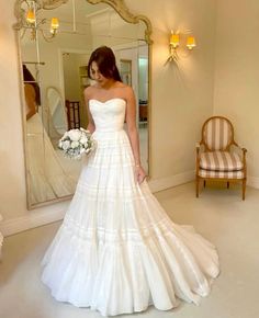 a woman standing in front of a mirror wearing a wedding dress with tiered layers