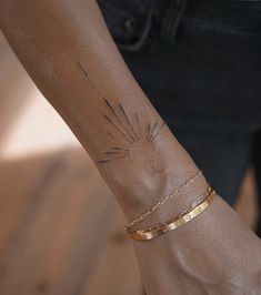 a woman's arm with a gold bracelet and sunburst tattoo on it