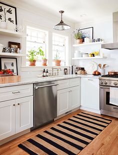 a clean kitchen with white cabinets and stainless steel stove top oven, dishwasher, sink, and rug