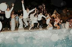 a group of people jumping in the air near a pool at night with balloons and streamers