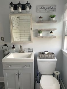 a white toilet sitting next to a sink in a bathroom under a mirror and shelves