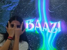 a woman covering her face in front of a neon sign that says baaz on it