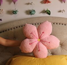 a pink flower pillow sitting on top of a bed next to a person's hand