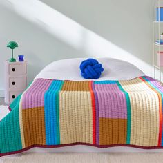 a bed with a multicolored quilt on top of it next to a white dresser