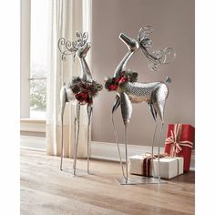 two metal reindeer statues with christmas decorations and presents in front of a window on a wooden floor