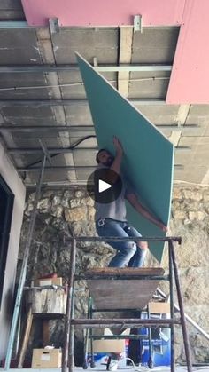 a man standing on top of a wooden stepladder holding up a green board