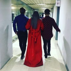 three people walking down a hallway together in long red dresses and blue shirts with their backs to the camera