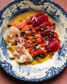 a blue and white plate topped with fish, capers and mustard sauce on top of a table