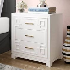 a white chest of drawers in a room with pink walls and wooden floors, flowers on top