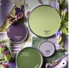 three different shades of green and purple paint with flowers on the table next to them