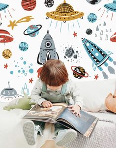 a little boy reading a book in front of a wall with rockets and planets on it