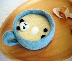 a small stuffed animal in a tea cup on a wooden tray next to some spoons