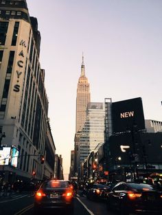 cars are driving down the street in front of tall buildings and skyscrapers at dusk