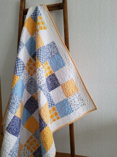 a blue and yellow quilt hanging from a wooden ladder in front of a white wall