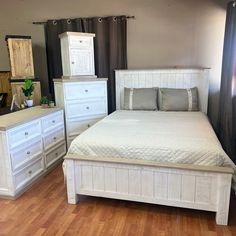 a white bed sitting in a bedroom next to two dressers and a mirror on top of a wooden floor